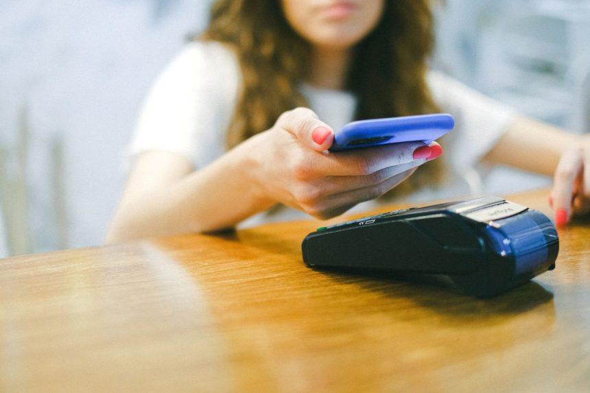 Mulher realiza um pagamento por aproximação com o celular em um terminal de pagamento.