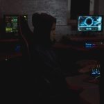 Profissional analisa dados em vários monitores em uma sala escura, em contexto de monitoramento de segurança cibernética.