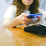 Mulher aproxima um smartphone de uma máquina para realizar um pagamento por aproximação.