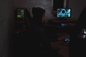 Profissional analisa dados em vários monitores em uma sala escura, em contexto de monitoramento de segurança cibernética.