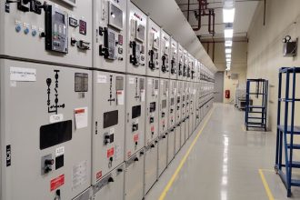 Sala de controle elétrico com uma longa fileira de painéis e equipamentos de monitoramento.