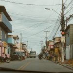 Rua movimentada com lojas locais e veículos em uma cidade brasileira.
