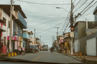 Rua movimentada com lojas locais e veículos em uma cidade brasileira.