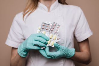 Profissional de saúde usando luvas segura cartelas de medicamentos em um ambiente de atendimento.
