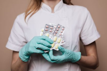 Profissional de saúde usando luvas segura cartelas de medicamentos em um ambiente de atendimento.