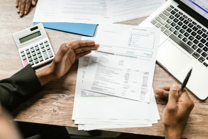 Mãos analisam documentos financeiros ao lado de uma calculadora e um laptop sobre uma mesa de escritório.